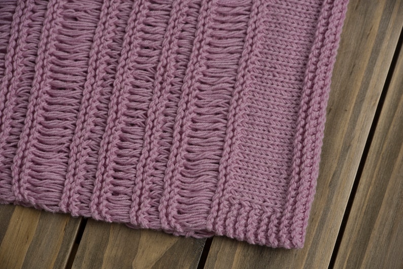 Close-up of a light pink hand knit summer sweater top with stockinette, garter stitch and three kinds of drop stitches.
