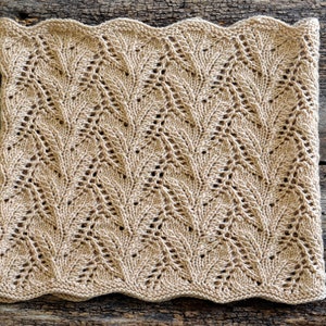 May include: A beige knitted scarf with a delicate leaf pattern. The scarf has a wavy edge and is made with a soft yarn.