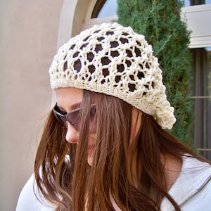 Puede incluir: Un gorro blanco de ganchillo con un patrón de encaje. El gorro lo lleva una persona con el pelo largo y castaño y gafas de sol.