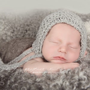 Infant boy wears a light gray knit garter stitch bonnet hat. Beginner knitting pattern.