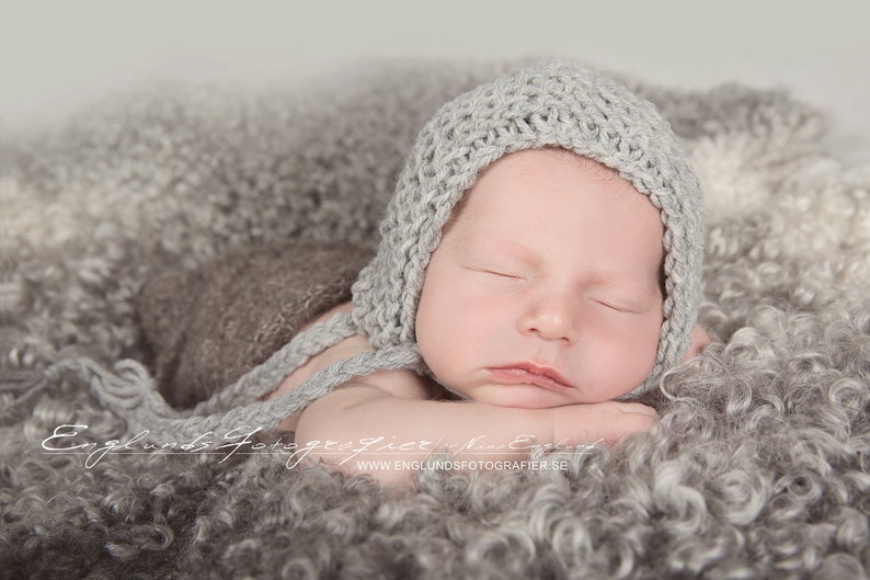 Infant boy wears a light gray knit garter stitch bonnet hat. Beginner knitting pattern.