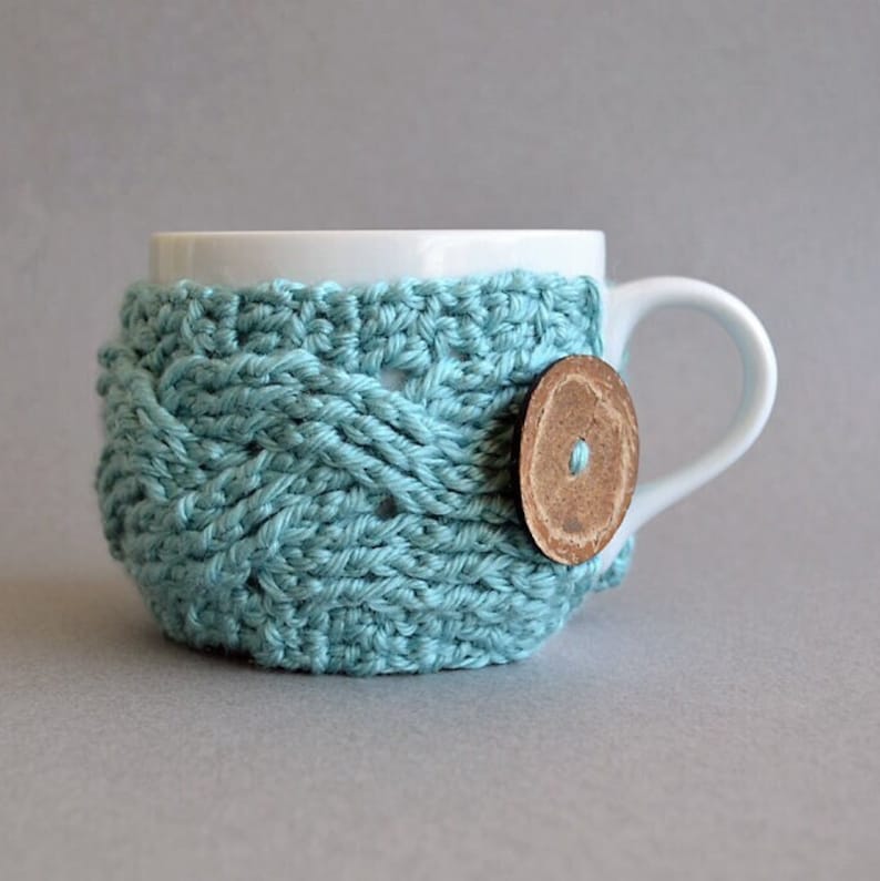 Easy crochet pattern for a cable crocheted cup cozy with a big button. This crocheting tutorial is a perfect gift to learn how to crochet cables.