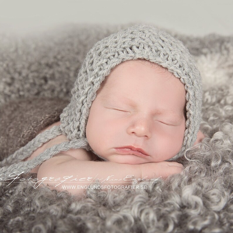 Newborn boy wearing a classic garter stitch baby bonnet with ties and tassels. This is an easy, beginner-friendly knitting pattern.