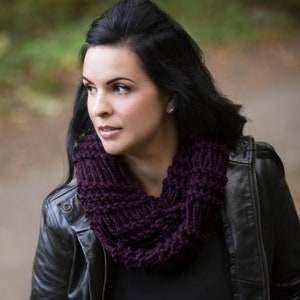 Puede incluir: Una mujer con una bufanda de punto infinita de color morado oscuro y una chaqueta de cuero negra.
