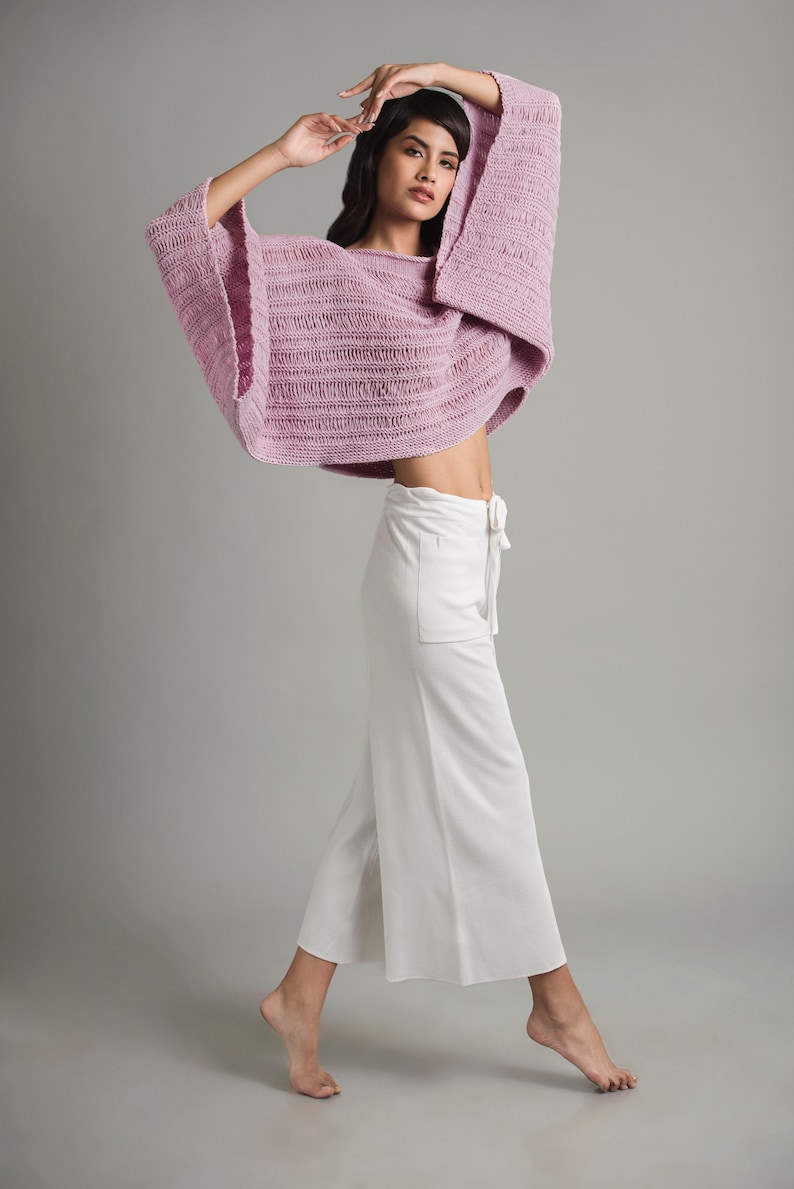 A young girl is wearing a light pink knit summer boatneck sweater with wide sleeves. The sweater features stockinette, garter stitch and three types of drop stitches.