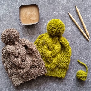 Könnte beinhalten: Zwei gestrickte Mützen mit Bommeln. Eine Mütze ist braun und die andere grün.