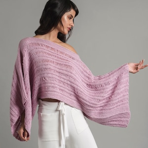 Puede incluir: Un suéter de punto de color lila claro con un corte holgado y de gran tamaño, con un escote amplio y abierto. El suéter está hecho de un hilo suave y ligero y tiene un estilo relajado y casual.