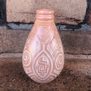 May include: A small, brown ceramic bottle with a white geometric design. The bottle has a rounded bottom and a narrow neck.