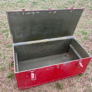 May include: A vintage red wooden storage chest with a hinged lid. The lid is open, revealing the interior of the chest, which is lined with green wood. The chest has metal hinges and clasps.