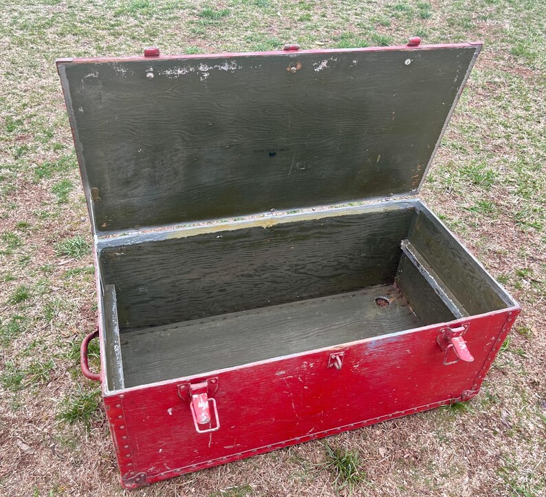 May include: A vintage red wooden storage chest with a hinged lid. The lid is open, revealing the interior of the chest, which is lined with green wood. The chest has metal hinges and clasps.