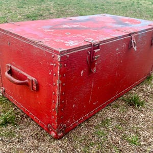 May include: A vintage red wooden storage chest with metal hardware and a handle. The chest has a distressed finish and is secured with metal clasps.