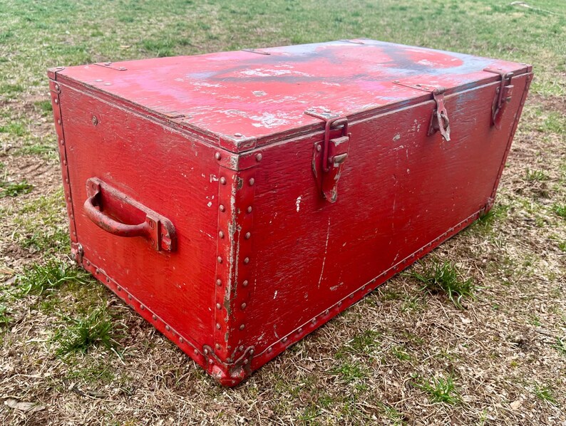 May include: A vintage red wooden storage chest with metal hardware and a handle. The chest has a distressed finish and is secured with metal clasps.