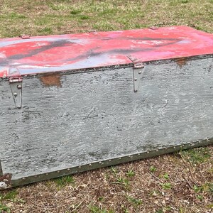 May include: A vintage wooden storage chest with a distressed gray paint finish and red paint accents. The chest has metal hinges and a latch.