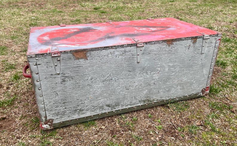 May include: A vintage wooden storage chest with a distressed gray paint finish and red paint accents. The chest has metal hinges and a latch.