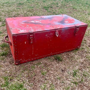 May include: A red wooden storage chest with metal hardware and a worn, distressed finish. The chest has a hinged lid and a handle on the side.