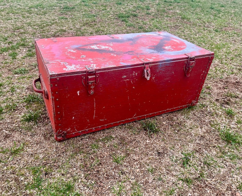 May include: A red wooden storage chest with metal hardware and a worn, distressed finish. The chest has a hinged lid and a handle on the side.