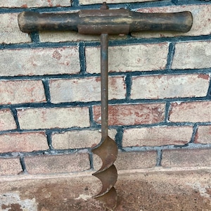 May include: An antique hand auger drill with a wooden handle and a metal bit. The drill is made of metal and has a spiral design on the bit. The handle is dark brown and the metal has a rusty appearance. The tool is designed for drilling holes.