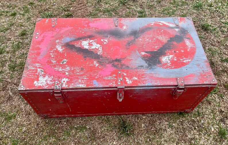 May include: A red wooden storage chest with a hinged lid and metal clasps. The chest has a distressed paint finish with faded blue and black paint accents.