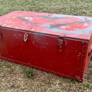 May include: A vintage red wooden storage chest with metal hardware and a worn, distressed finish. The chest has a hinged lid and metal clasps.