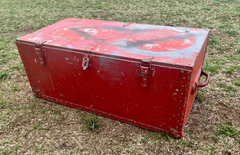 May include: A vintage red wooden storage chest with metal hardware and a worn, distressed finish. The chest has a hinged lid and metal clasps.