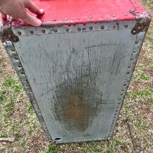 May include: A vintage red and gray wooden storage trunk with metal accents and rivets. The trunk has a hinged lid and a metal handle.