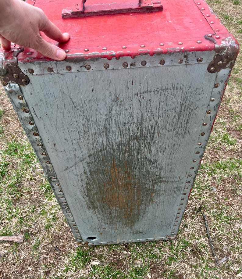 May include: A vintage red and gray wooden storage trunk with metal accents and rivets. The trunk has a hinged lid and a metal handle.