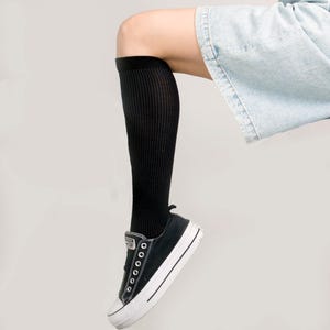 May include: A person wearing black knee-high socks and black and white sneakers with a white platform sole. The person is wearing denim shorts.