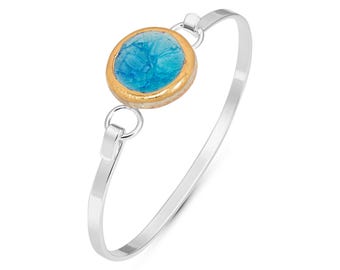 May include: A silver bangle bracelet with a round blue glass charm with a gold rim. The charm has a textured surface.