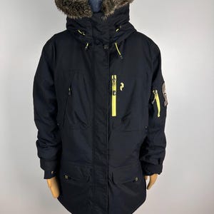 Könnte beinhalten: Schwarzer Winterparka mit Kapuze mit Kunstfellfutter und gelben Reißverschlüssen. Die Jacke hat mehrere Taschen und einen Logoaufnäher am Ärmel. Ein stilvolles und funktionelles Oberbekleidungsstück.