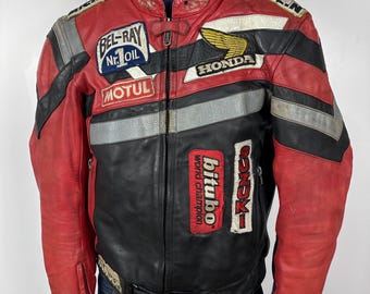 May include: A red and black leather motorcycle jacket with various patches, including "Bel-Ray No. 1 Oil", "Motul", "Honda", "Michelin", and "Bitubo World Champion".