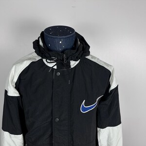 May include: A black and white jacket with a blue Nike swoosh logo. The jacket has a zipper closure and a hood.