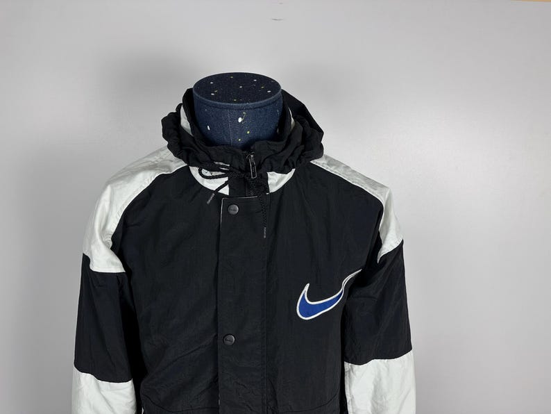 May include: A black and white jacket with a blue Nike swoosh logo. The jacket has a zipper closure and a hood.