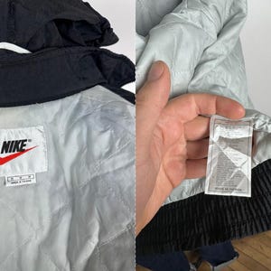 May include: Black Nike windbreaker jacket with a white lining and a Nike logo on the left chest. The jacket has a zipper closure and a hood. The tag says "Nike" and "Made in Taiwan".