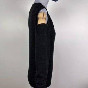 May include: A dark gray sweater with long sleeves and a crew neck. The sweater has a unique design with cut-out details on the shoulders. The sweater is worn over a striped collared shirt. The mannequin is wearing a dark blue face mask with white dots.