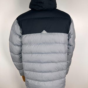 Puede incluir: Chaqueta acolchada gris y negra con capucha. La chaqueta tiene una secci&oacute;n superior y capucha negras, con un peque&ntilde;o logotipo blanco. La secci&oacute;n inferior es gris y acolchada. Dise&ntilde;ada para la calidez y actividades al aire libre.