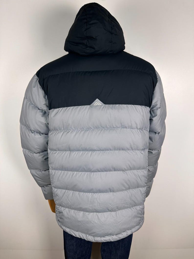 Puede incluir: Chaqueta acolchada gris y negra con capucha. La chaqueta tiene una secci&oacute;n superior y capucha negras, con un peque&ntilde;o logotipo blanco. La secci&oacute;n inferior es gris y acolchada. Dise&ntilde;ada para la calidez y actividades al aire libre.