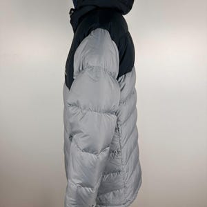 Puede incluir: Chaqueta acolchada con capucha de dos tonos. La parte superior y la capucha son negras, contrastando con el cuerpo gris claro. La chaqueta presenta un dise&ntilde;o acolchado y un cuello alto. Dise&ntilde;ada para el fr&iacute;o, ofrece calidez y protecci&oacute;n. Ideal para el invierno.