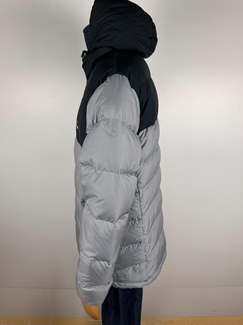 Puede incluir: Chaqueta acolchada con capucha de dos tonos. La parte superior y la capucha son negras, contrastando con el cuerpo gris claro. La chaqueta presenta un dise&ntilde;o acolchado y un cuello alto. Dise&ntilde;ada para el fr&iacute;o, ofrece calidez y protecci&oacute;n. Ideal para el invierno.