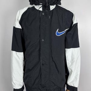 May include: Black and white windbreaker jacket with a blue Nike swoosh logo. The jacket has a hood and a zipper closure.