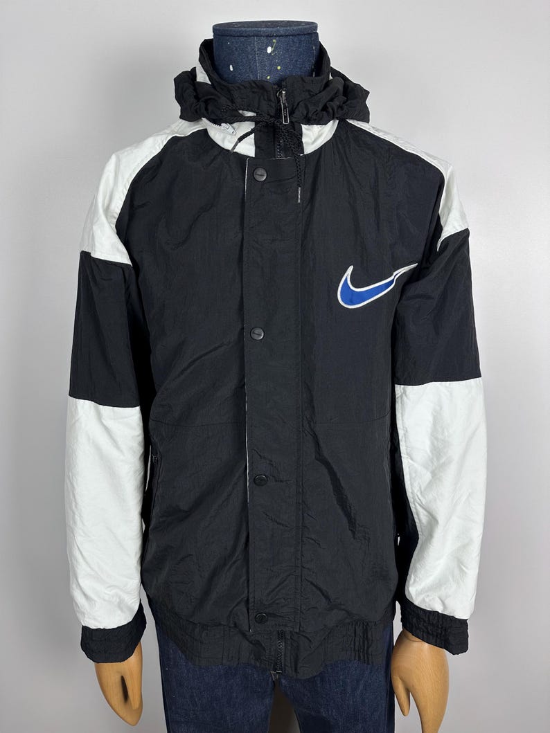 May include: Black and white windbreaker jacket with a blue Nike swoosh logo. The jacket has a hood and a zipper closure.