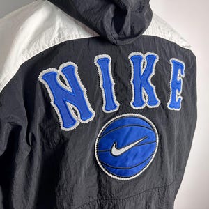 May include: Black and white windbreaker jacket with a blue and white Nike logo and the word "NIKE" in blue with a white outline.