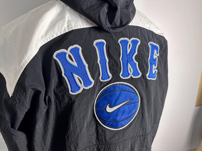 May include: Black and white windbreaker jacket with a blue and white Nike logo and the word "NIKE" in blue with a white outline.