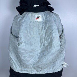 May include: Black Nike puffer jacket with a white Nike logo and a white tag that says "Nike" on it. The jacket has a quilted lining.