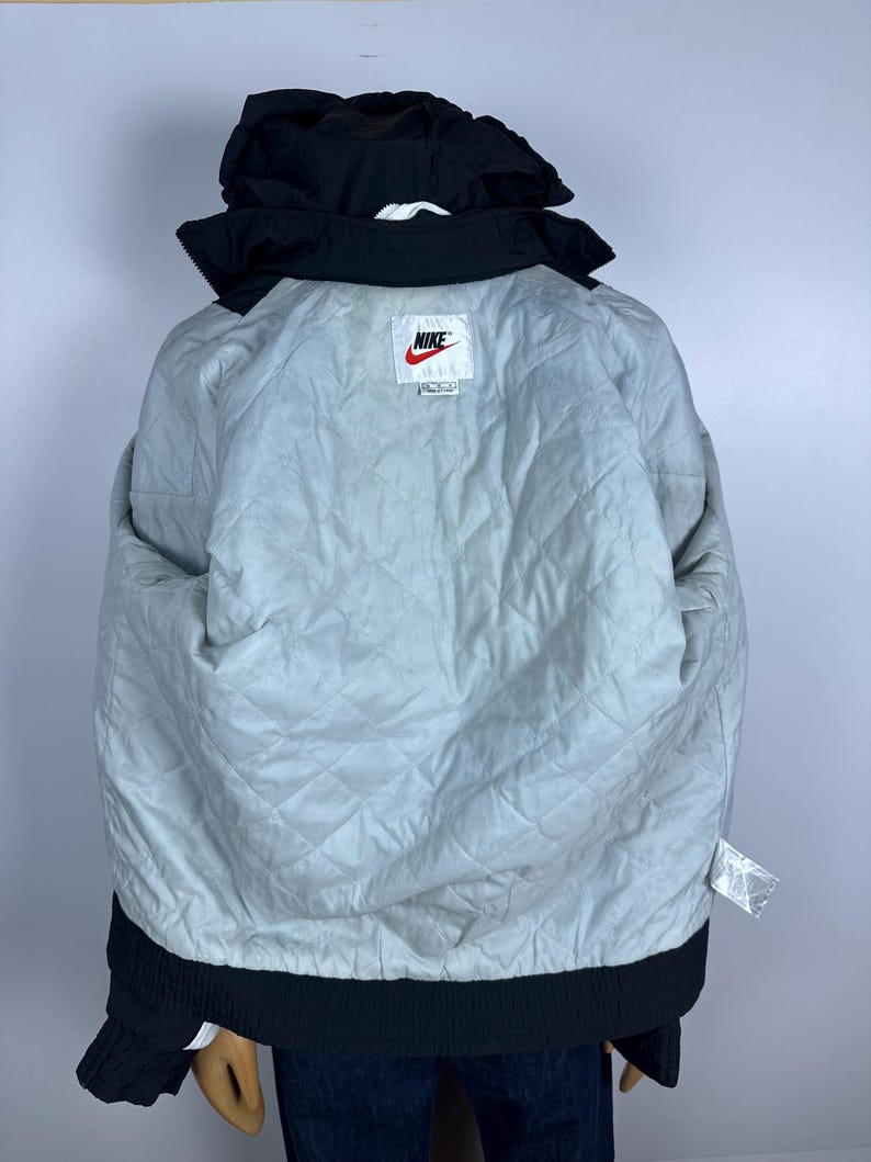 May include: Black Nike puffer jacket with a white Nike logo and a white tag that says "Nike" on it. The jacket has a quilted lining.