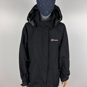 May include: Black Berghaus hooded jacket with a zipper closure. The jacket has a small Berghaus logo in red, white, and blue on the chest. The jacket has a hood and long sleeves. The jacket is displayed on a mannequin.