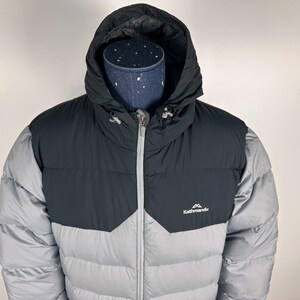 Puede incluir: Chaqueta acolchada con capucha gris y negra, con cremallera completa y el logotipo "Kathmandu". La chaqueta tiene un dise&ntilde;o acolchado y un cuello alto para mayor calidez.