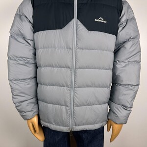 Puede incluir: Chaqueta acolchada gris y negra con cremallera completa. La chaqueta tiene una secci&oacute;n superior negra y una secci&oacute;n inferior gris. El logotipo de Kathmandu est&aacute; en la parte superior izquierda del pecho. Para clima fr&iacute;o.