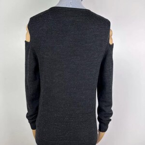 May include: Dark gray sweater with long sleeves and cut-out shoulder details. The sweater has a v-neck and is made of a soft, knitted material. The cut-out shoulder design adds a modern touch to the classic sweater style.