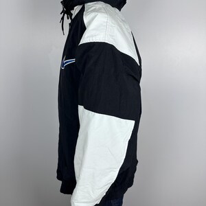 May include: A black and white windbreaker jacket with a blue swoosh logo. The jacket has a hood and a zipper closure.