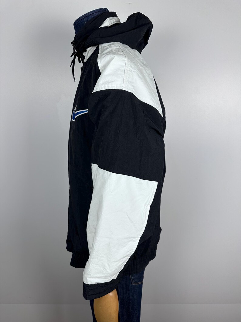 May include: A black and white windbreaker jacket with a blue swoosh logo. The jacket has a hood and a zipper closure.